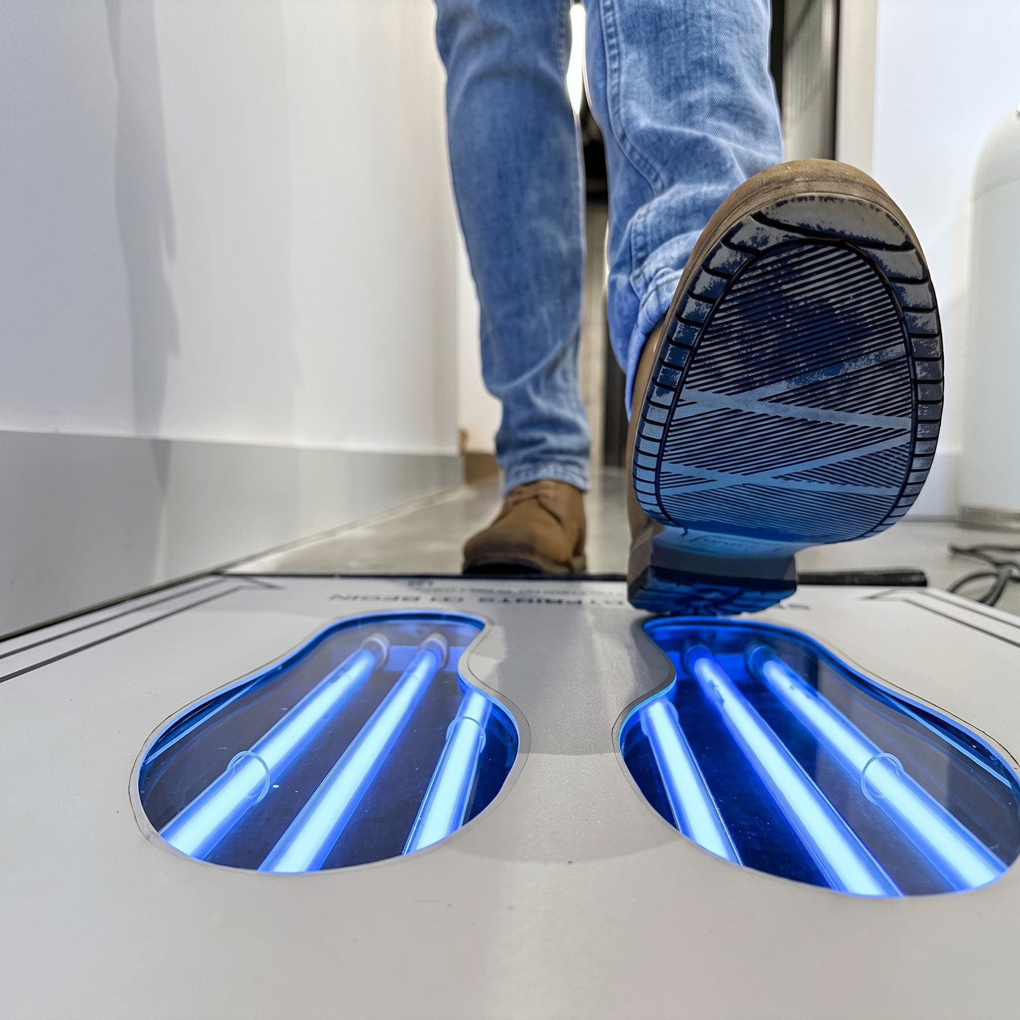 Shoe sole raised above the lit UVZone treatment wells at a facility entry.