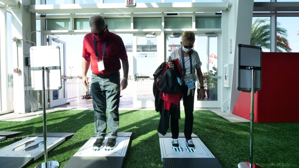 A man and woman stepping onto the PathO₃Gen Solutions' UVZone® Shoe Sanitizer before entering a building, promoting a clean and sanitary environment.